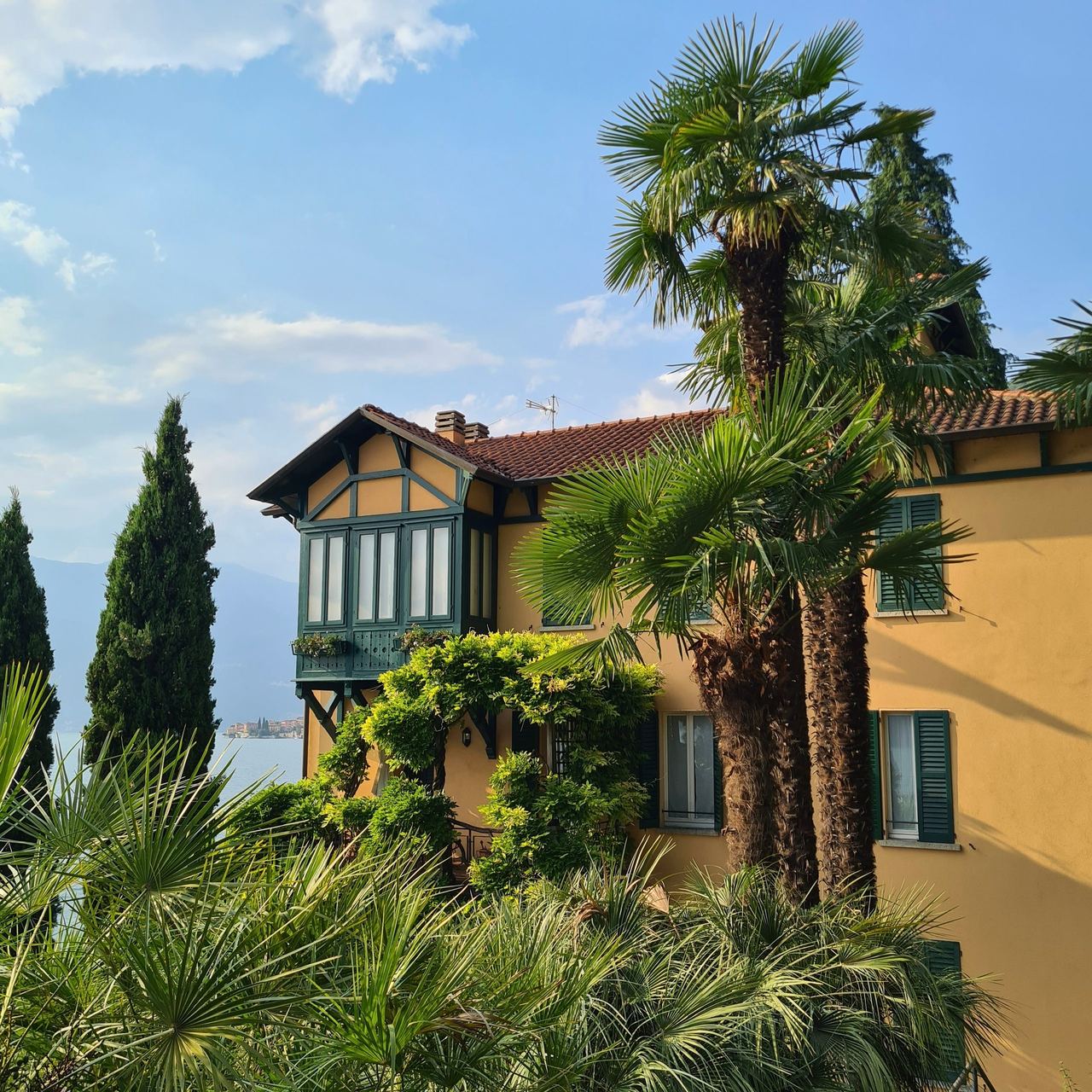 Sunlit Mediterranean-style villa with terracotta roof, palm trees, lush garden, and blue sky, creating a warm, peaceful atmosphere.