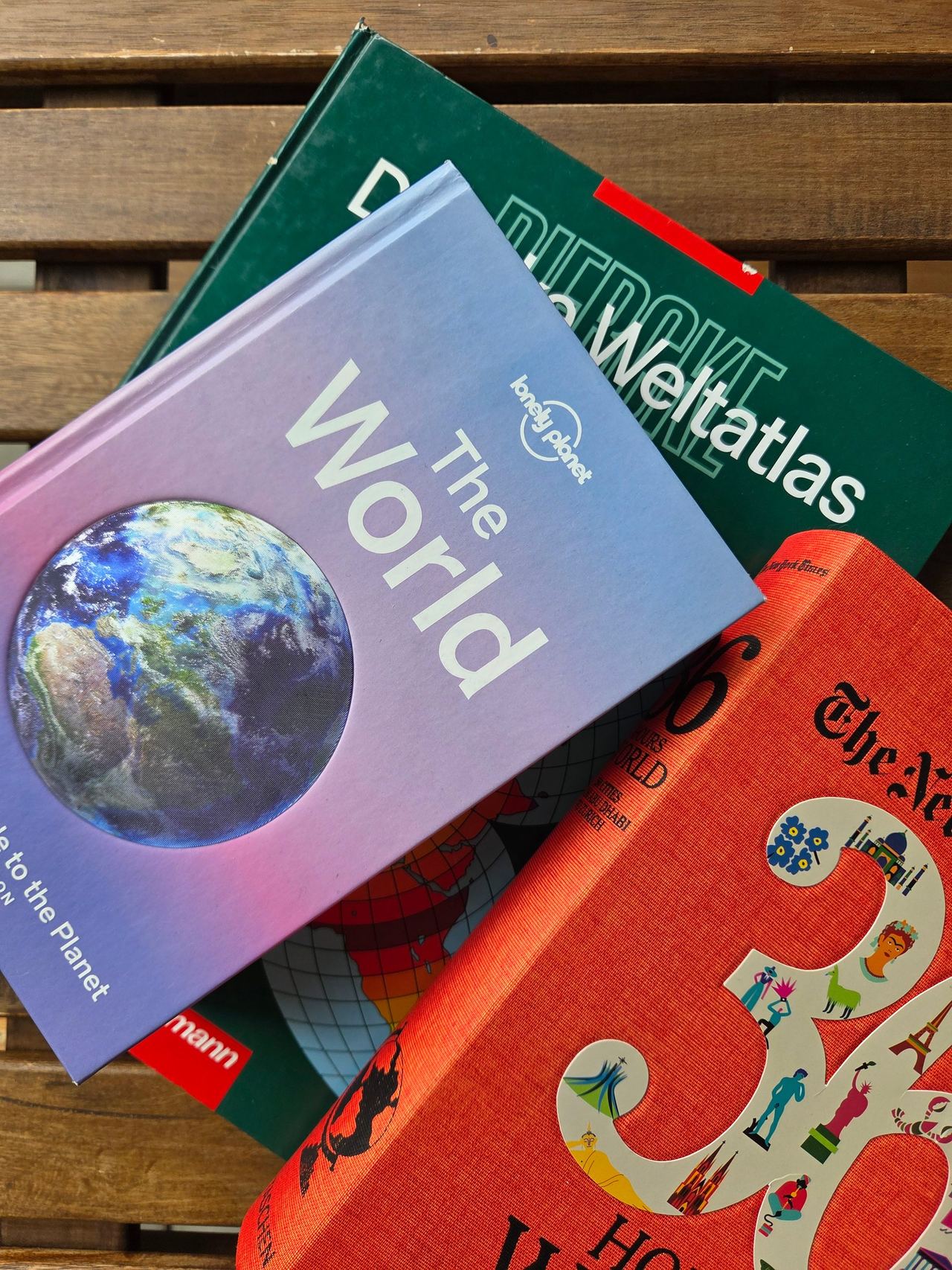 The travel guide books, and a world atlas stacked upon each other.