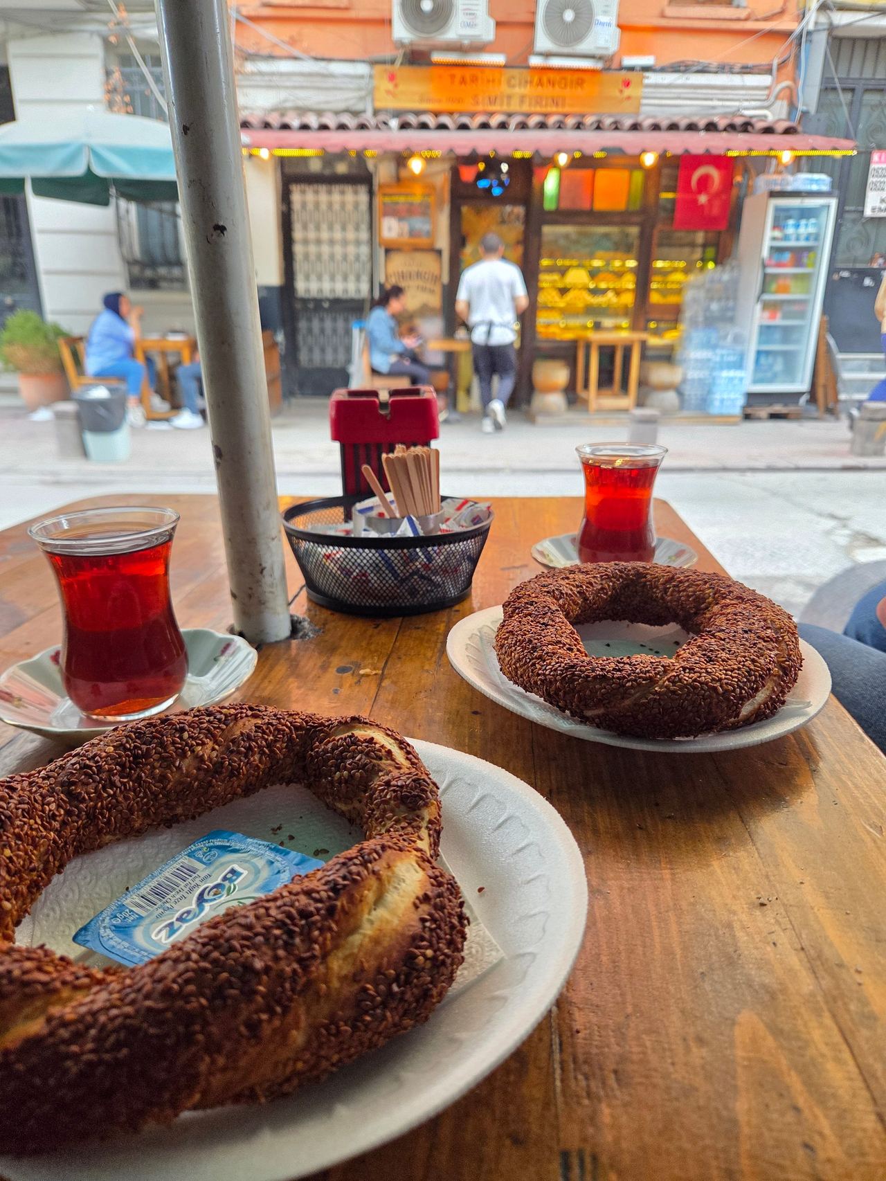 Turkish simit rings with glasses of tea sit on a wooden café table, overlooking a lively street-side bakery.