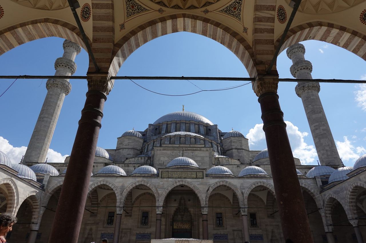 Süleymaniye Mosque, framed by ornate courtyard arches beneath a blue sky; serene and monumental.