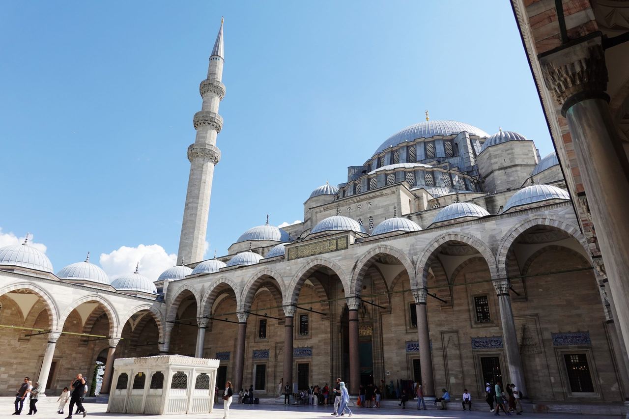 The Süleymaniye Mosque’s vast gray dome and slender minaret rise above a sunlit courtyard of stone arches.