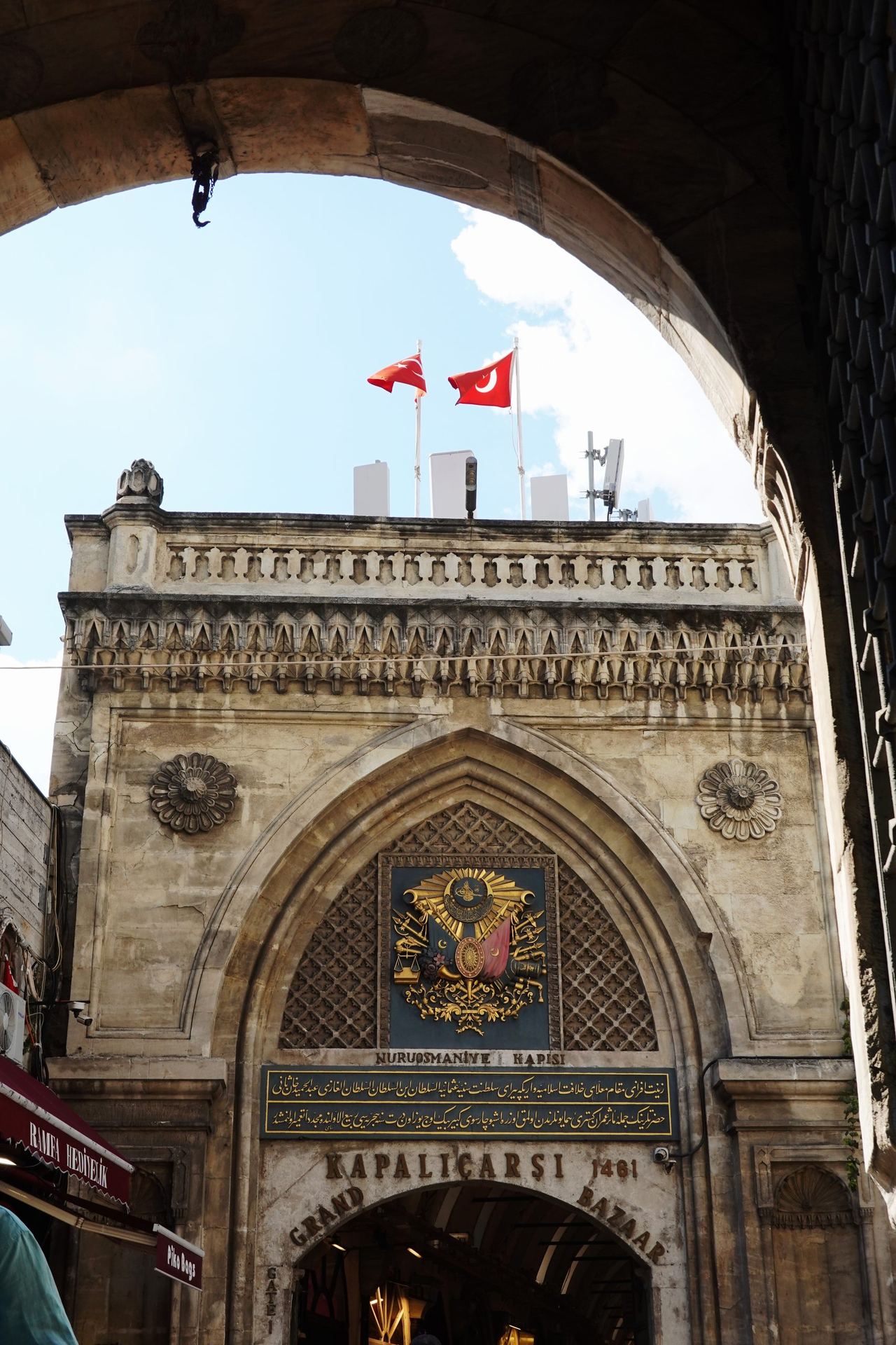 Ornate stone entrance to Kapalı Çarşı, Istanbul, framed by a dark arch; Turkish flags flutter above.