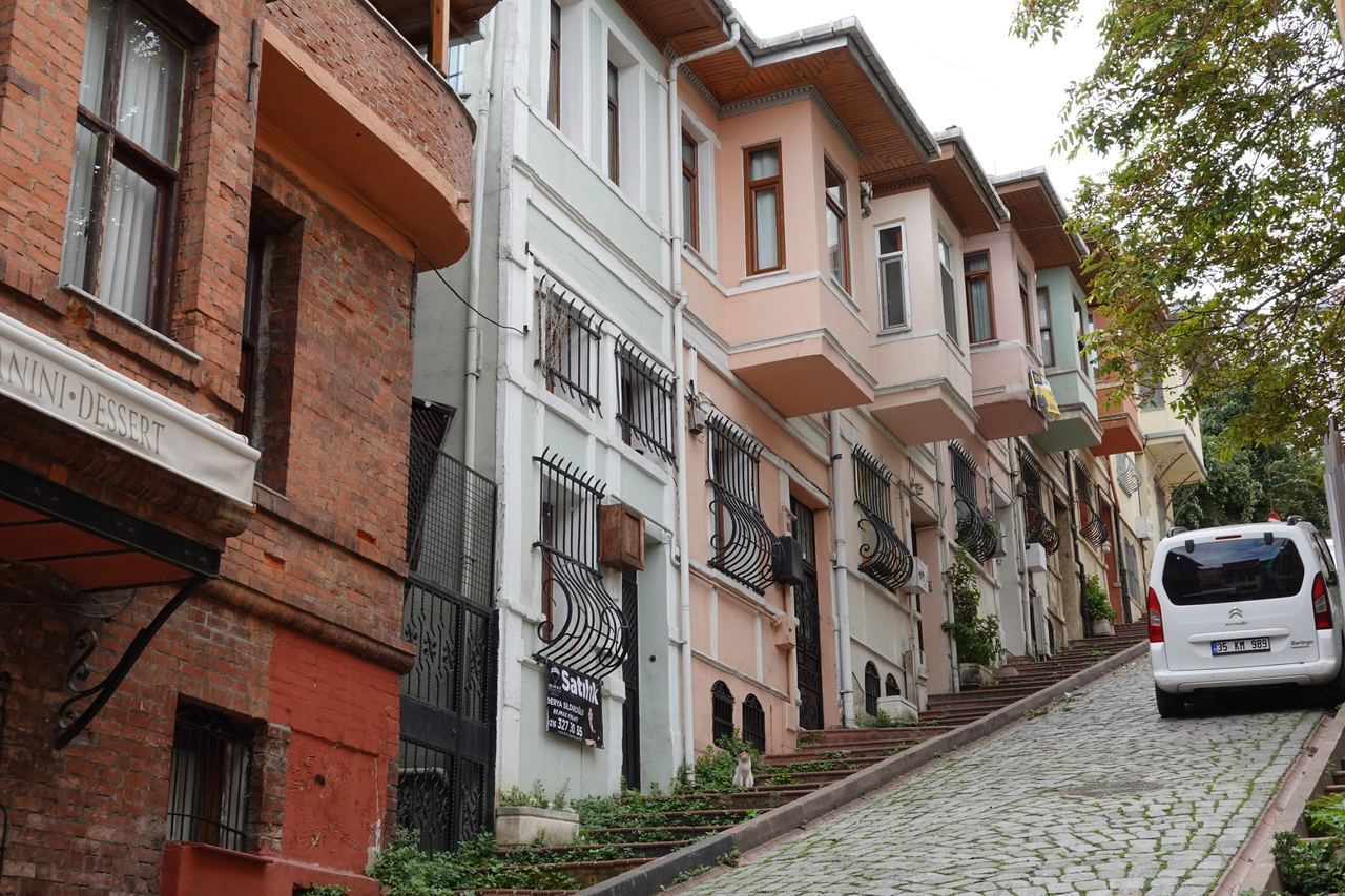 Merdivenli street climbs past historic red-brick and pastel homes with balconies; a quiet old-town neighborhood.