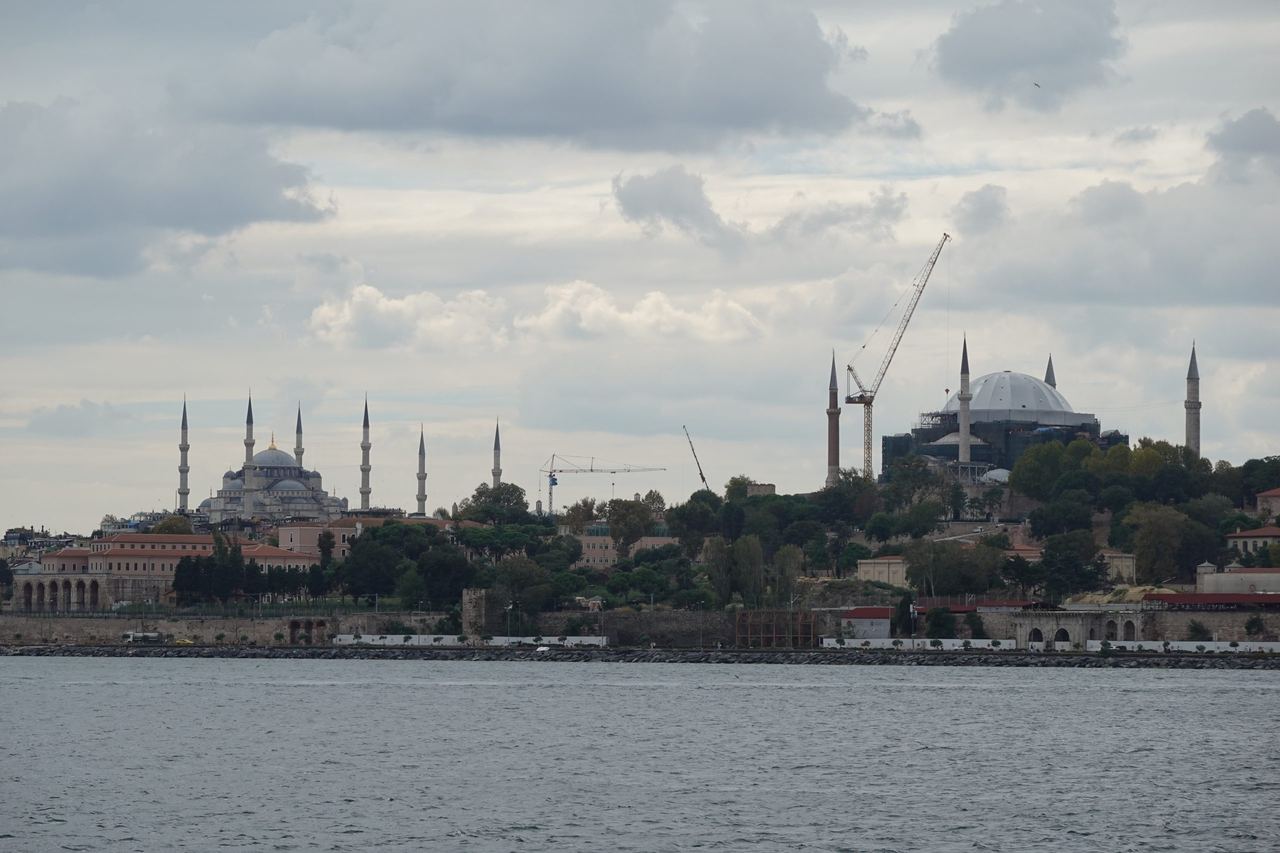 Istanbul’s historic skyline across the Bosphorus, with domed mosques and minarets beneath heavy clouds; cranes add a note of ongoing change.