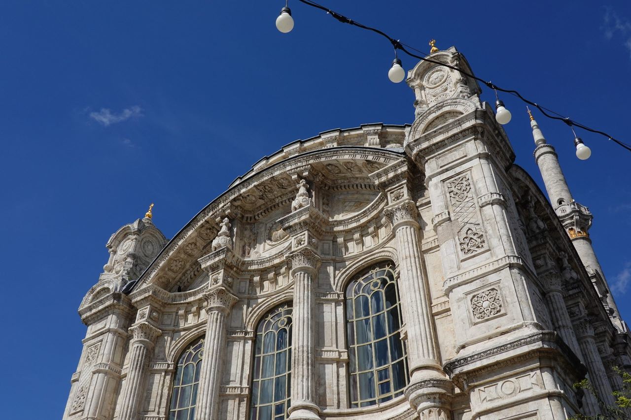 Low-angle view of Ortaköy Mosque beneath a vivid blue sky; festive lights add a calm grandeur.