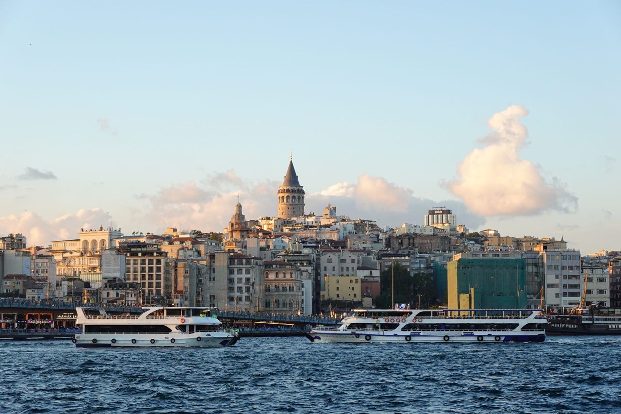 Istanbul’s waterfront glows in warm evening light as the Galata Tower rises above the city and passenger ferries cross the choppy Bosphorus.