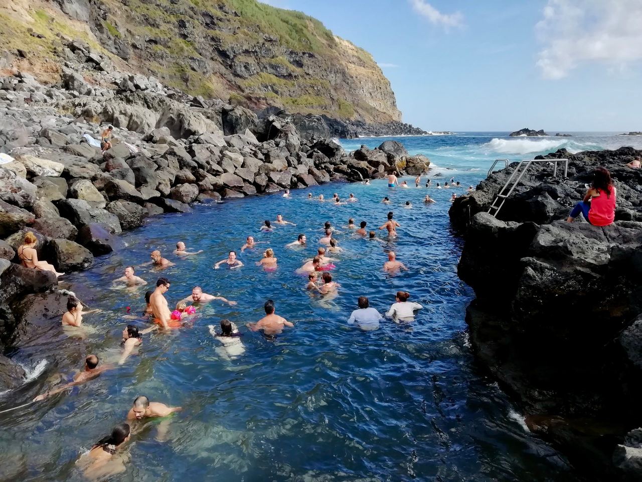 Natural pool with swimmers on a rocky shore in Ferraria
