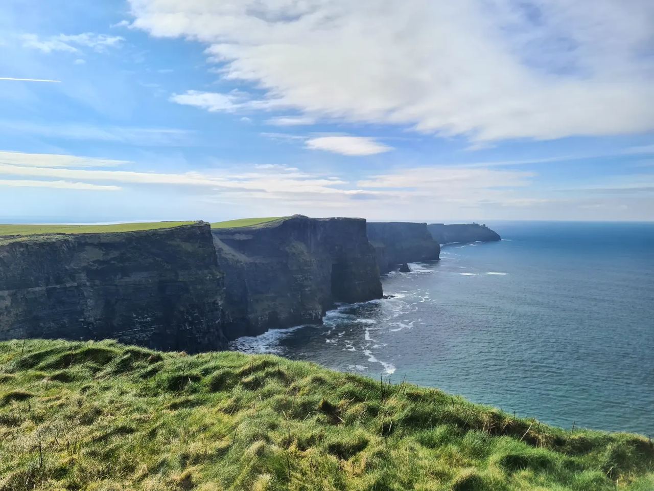 Line of sea cliffs next to the water covered with grass on sunny day